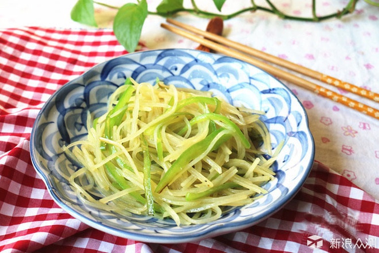 一张餐桌上的白色瓷盘中盛放着一盘金黄色边缘微焦的炒土豆丝,旁边配有红椒丝点缀,整体色泽诱人,背景虚化的家庭用餐环境营造温馨氛围 图片描述