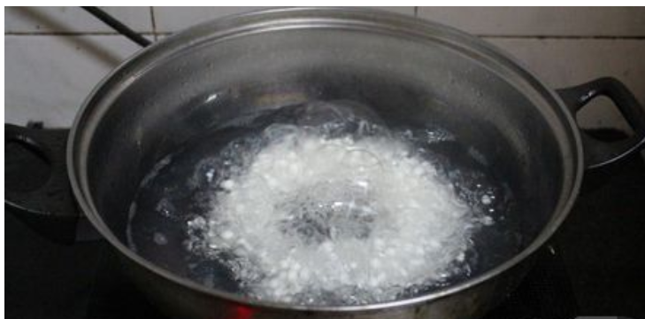 一位厨师正在灶台前操作,手持汤勺搅拌砂锅中的白扁豆汤,锅内可见漂浮的豆粒与胡萝卜块,蒸汽升腾,背景为中式厨房环境,突出家庭烹饪场景 白扁豆煲汤烹饪过程图