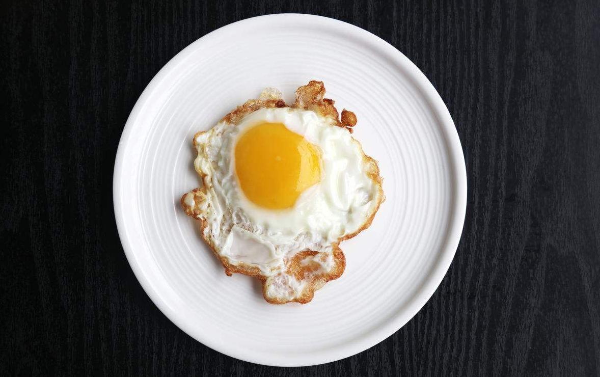 一枚新鲜的鸡蛋被横向切开,清晰展示蛋白透明凝胶状质地与橙黄色饱满蛋黄的分层结构,背景为白色瓷盘,光线柔和自然,突出食材原生态质感 鸡蛋剖面特写