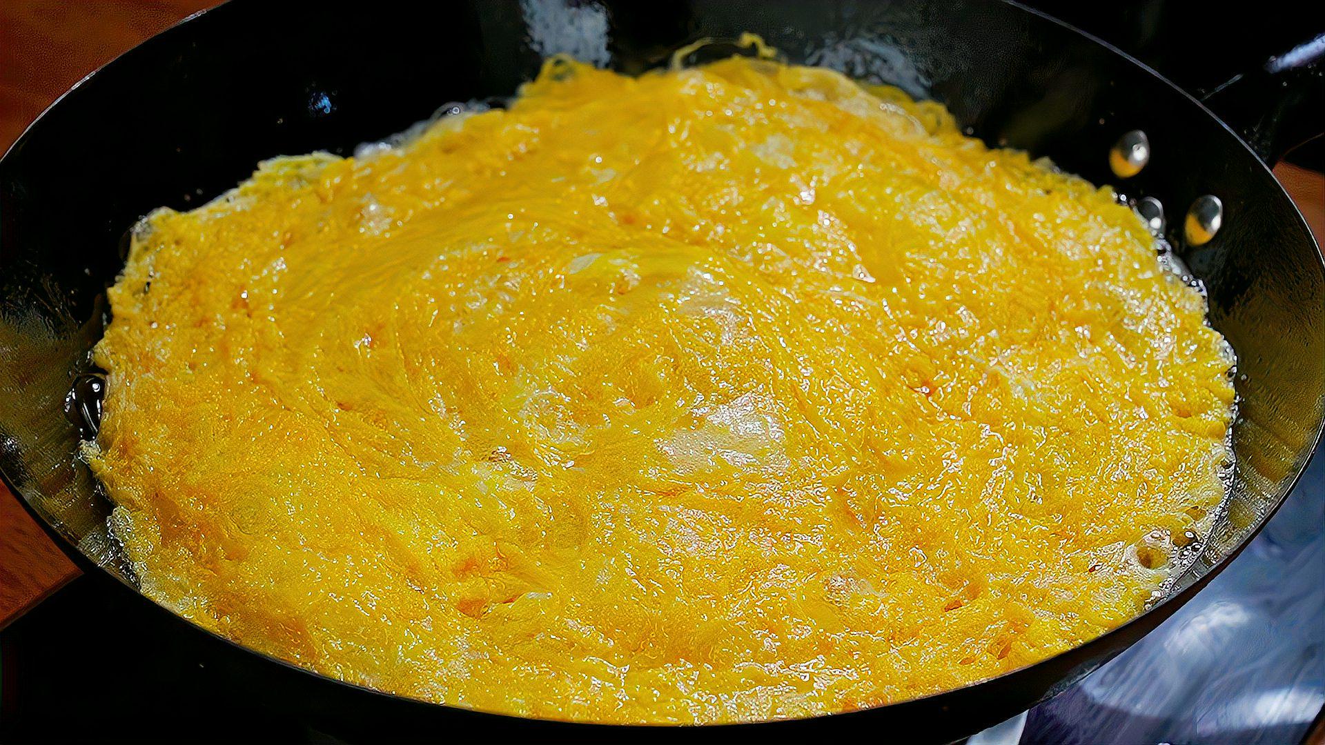 厨师正在用锅铲轻柔翻炒刚倒入蛋液的平底锅，蛋液呈半流动状态开始凝结，锅边略带焦黄香气