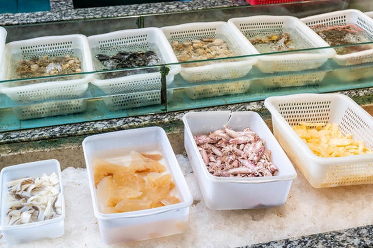 海鲜摊位上摆放着多条新鲜红鱿鱼,摊主正在整理货品,背景为湿漉漉的地面和冷藏展示柜,体现其作为生鲜农产品的流通环节 市场销售场景图