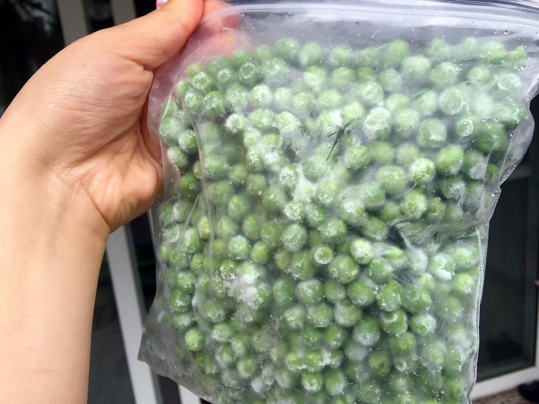 一个现代家庭厨房场景,女性正在将处理好的豌豆分装进透明密封袋,桌上摆放着标签笔、封口机和多个已封装的小袋豌豆,背景为嵌入式冰箱,其中冷冻抽屉可见整齐排列的冷冻食品,光线自然柔和 家庭厨房中冷冻豌豆分装存储场景