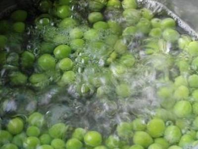 一名厨师正在案板上用手撕去荷兰豆两侧的老筋,旁边摆放着已处理好的翠绿荷兰豆条;另一侧是沸水中焯烫的荷兰豆,水面泛起轻微气泡,水中漂浮着几片绿叶 荷兰豆去筋与焯水过程