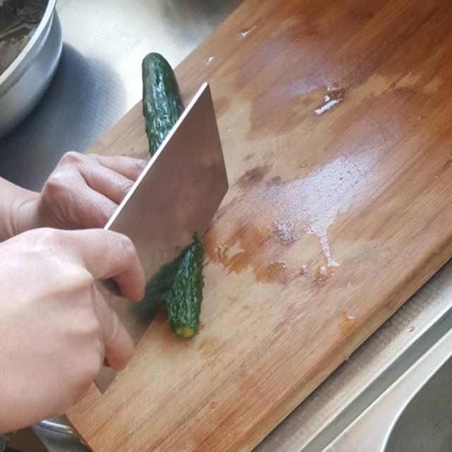 一名厨师正在操作台上用清水冲洗新鲜的小黄瓜,旁边摆放着干净的砧板和刀具,几根已切半的小黄瓜整齐排列,背景为明亮厨房环境 小黄瓜清洗与切割过程