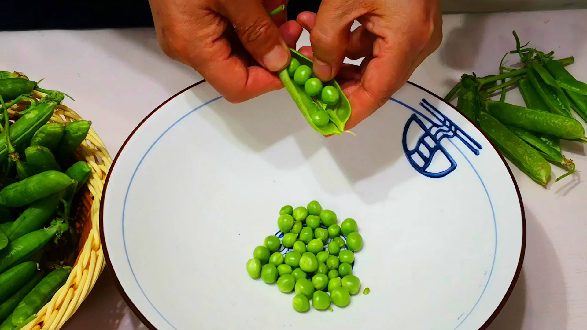 一位厨师正在桌面上逐一为甜豌豆去筋,手指动作清晰,展示如何从豆荚顶端开始撕下两侧纤维筋,背景为整洁厨房环境,强调操作的规范性与实用性 甜豌豆去筋手法演示图