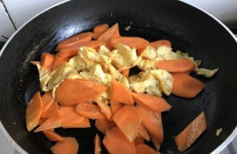 锅中正在翻炒胡萝卜与蘑菇，食材呈金黄色，表面微焦，蒸汽升腾，厨师手持锅铲操作