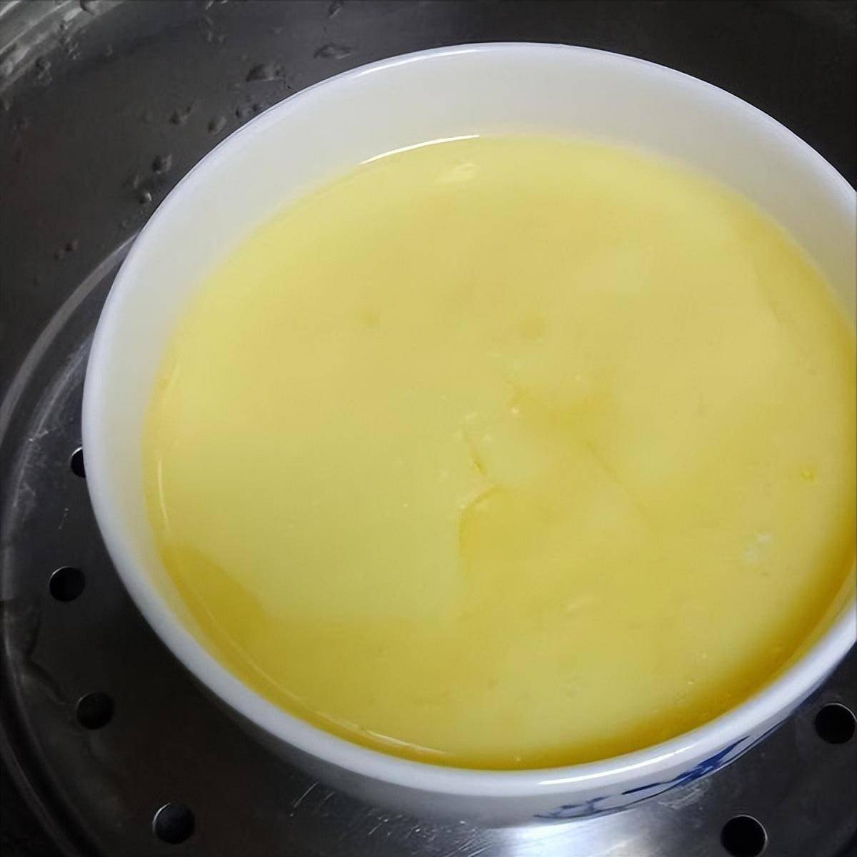 透明玻璃碗中装有刚蒸好的鸡蛋羹,旁边摆放着鸡蛋壳和蒸锅,背景为厨房环境 蒸蛋制作过程