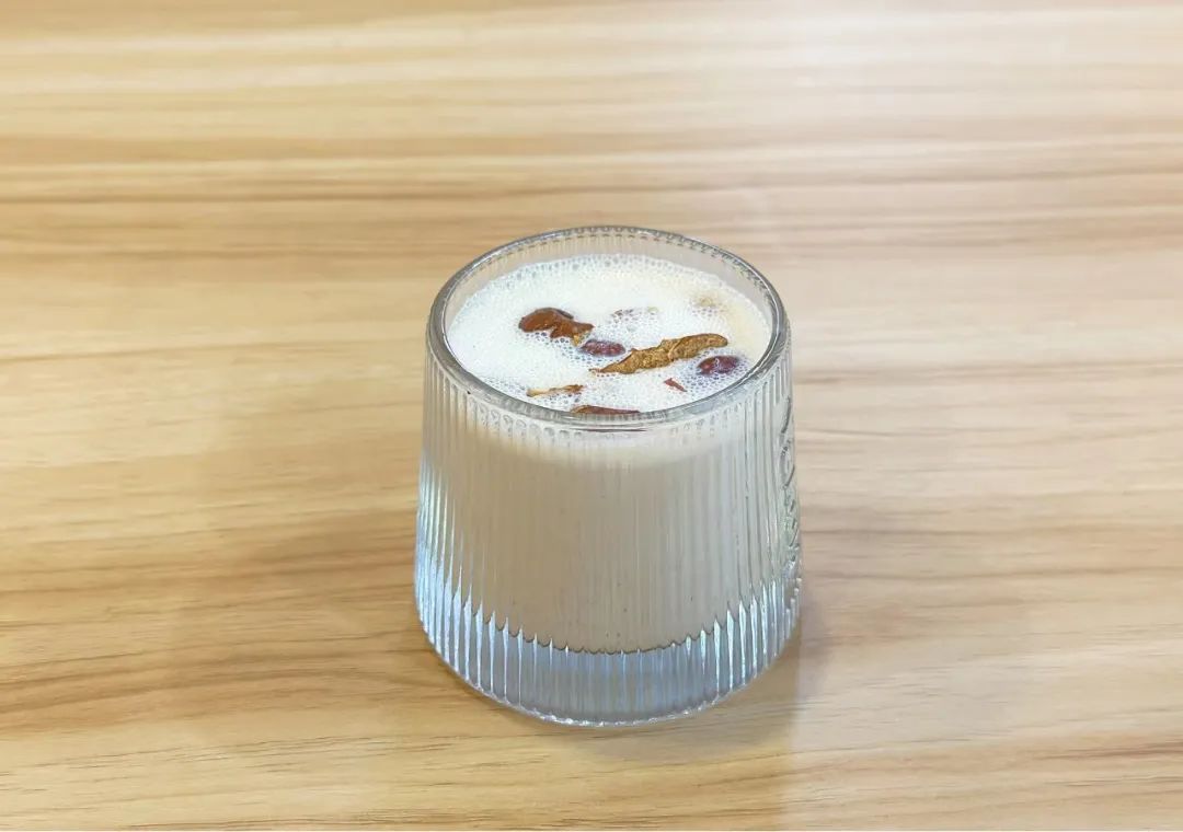 一杯金黄色的青枣酒被缓缓倒入透明玻璃酒杯中,液体清澈透亮,背景为木纹桌面与几颗完整的青枣,营造出自然健康的氛围 青枣酒成品倒出特写