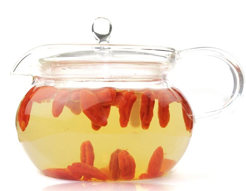 一个透明玻璃茶壶中正在冲泡的茶饮:金丝皇菊完全盛开,呈金黄色球状悬浮于水中;周围漂浮着红褐色的山楂片和暗红色的枸杞颗粒;茶汤整体呈现淡琥珀色,清澈透亮;热气微微上升,背景为简约中式茶席,配有竹制茶托与茶匙 玻璃壶中正在冲泡的金丝皇菊山楂枸杞茶