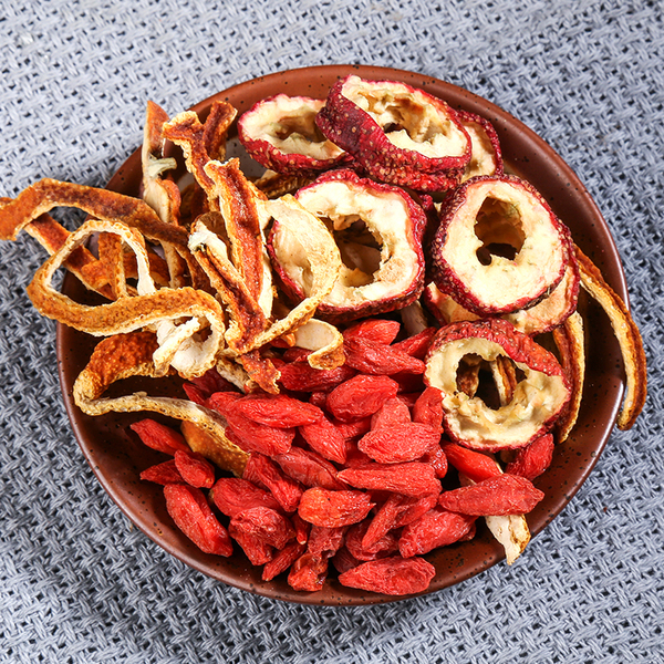 一个白色陶瓷小锅正在炉灶上慢火熬煮草本茶饮,锅内可见山楂干、陈皮、荷叶碎片等材料浸泡在红褐色液体中,旁边放置木勺和玻璃杯,展现家庭养生煮茶的真实场景 山楂干与其他草本材料混合煮茶场景