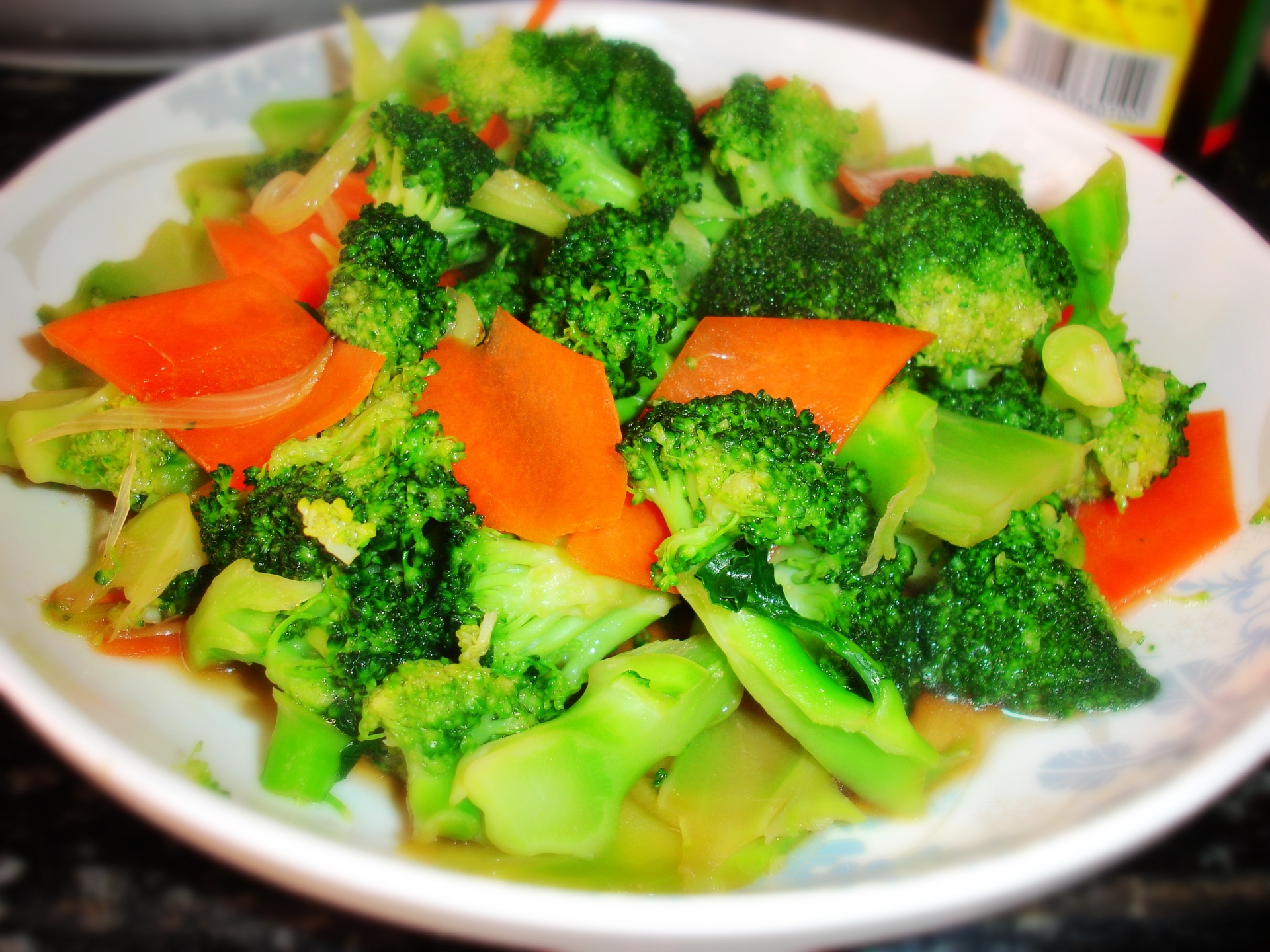 西兰花胡萝卜炒菜成品图,展示家庭常见做法 西兰花与胡萝卜混合炒制后的菜肴盛放在白色瓷盘中,旁边配有筷子和汤匙,背景为浅色木质餐桌