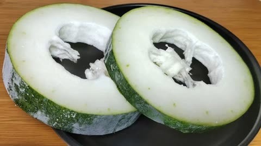 一个被纵向切开的冬瓜放置在白色瓷盘中,露出晶莹透明的果肉和黑色种子,背景简洁,突出内部结构与水分饱满感 冬瓜切开剖面图