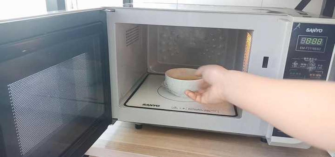 一台家用微波炉内部放置一个白色陶瓷碗,碗中整齐摆放着几颗已划十字口的栗子,蒸汽微微上升,显示刚加热完毕的状态 微波炉加热栗子