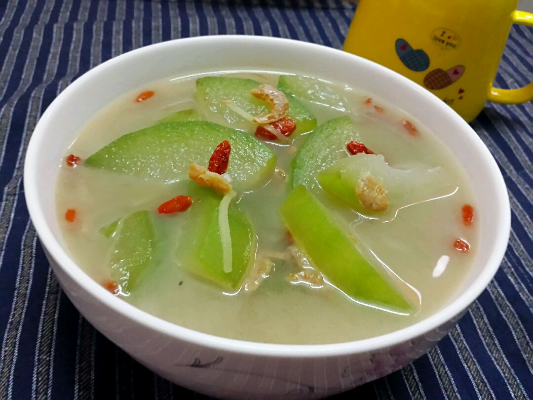 一碗清淡的冬瓜汤,汤色清澈,冬瓜片呈半透明状,旁边摆放新鲜冬瓜和配料如薏仁 冬瓜汤特写