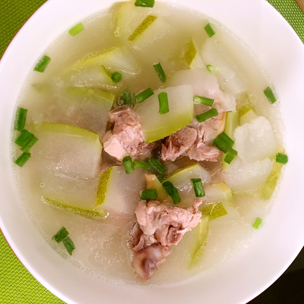 一碗热气腾腾的冬瓜排骨汤盛放在白色瓷碗中,汤色清澈,可见漂浮的枸杞与姜片,冬瓜块半透明状,排骨沉底,旁边摆放一双木筷,背景为简约中式餐桌,营造温馨家常氛围 冬瓜排骨汤成品展示