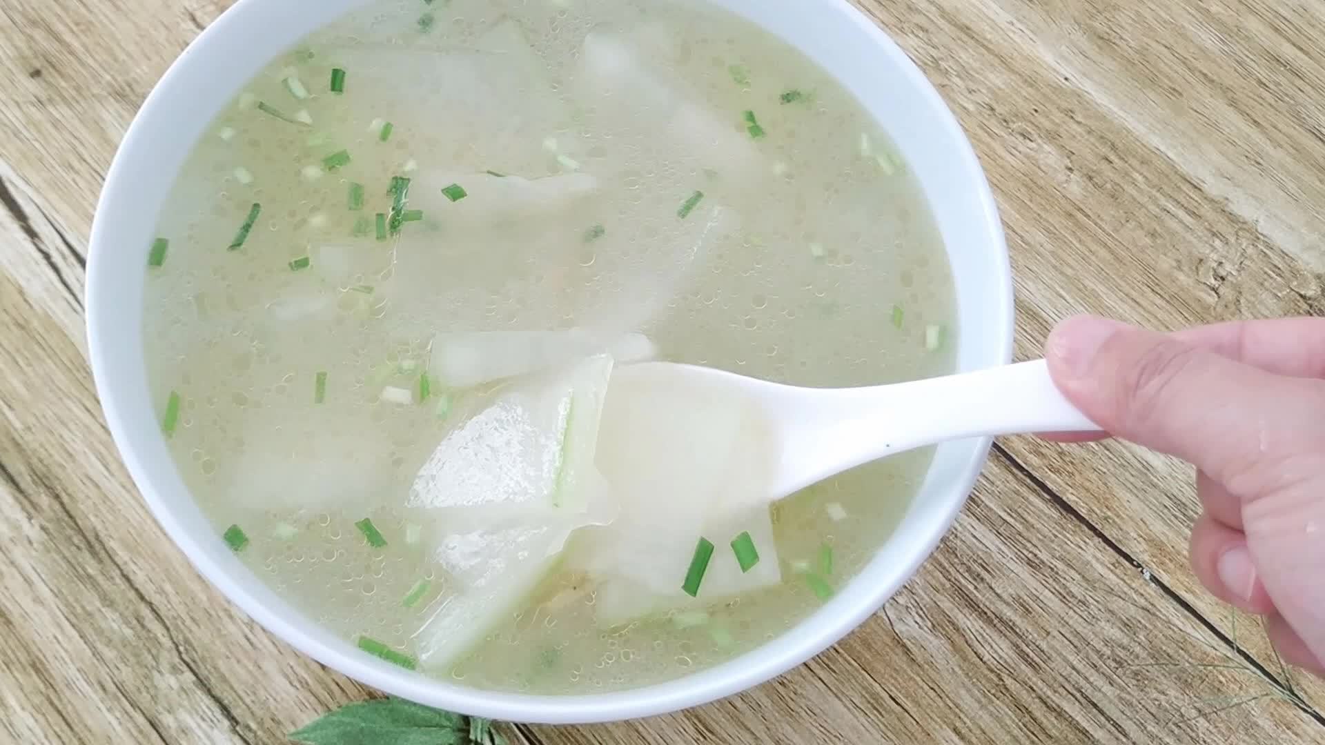 白色冬瓜块在透明清汤中漂浮,汤色清澈无油,旁边配有葱花点缀,碗边摆放一双木筷,体现健康饮食场景 冬瓜切片与清水汤品