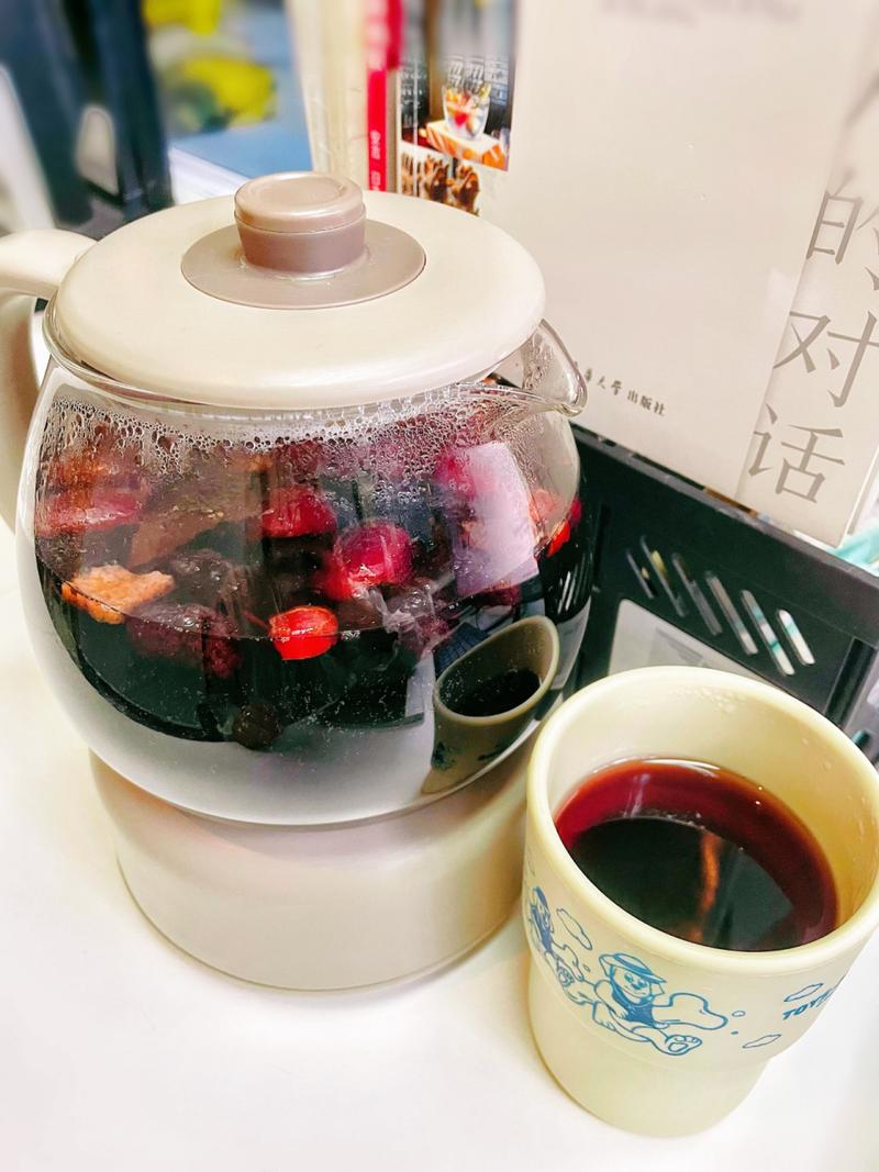 一位女性正在用玻璃茶壶冲泡北五味子,茶水中漂浮着暗红色果实,旁边摆放陶瓷茶杯和木质茶托,环境温馨自然,体现健康生活方式 北五味子茶饮冲泡场景