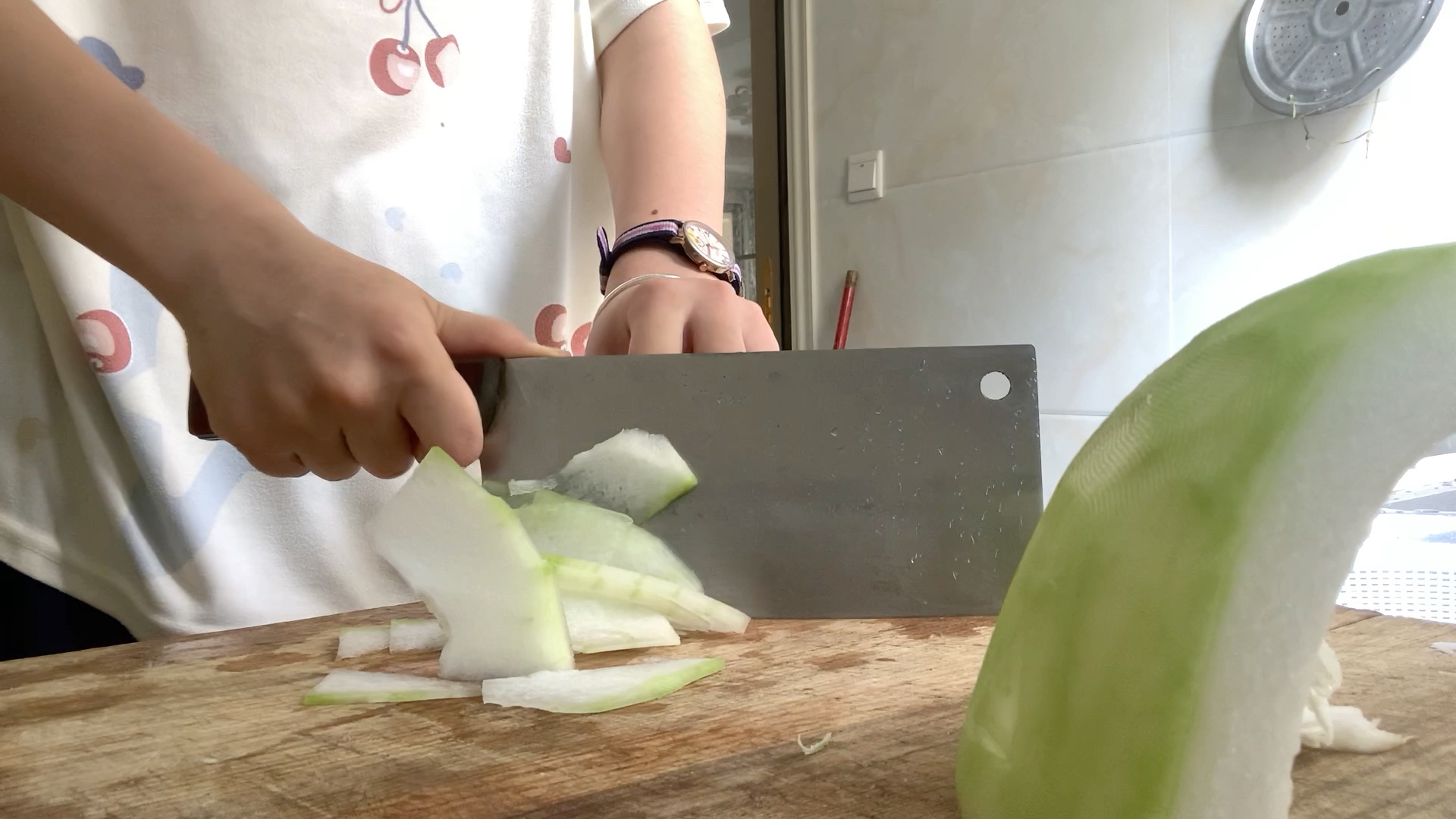 一位厨师正在厨房操作台上用刀具将白皮冬瓜切成均匀的块状,旁边放置着去皮工具和清洁毛巾,背景为明亮的厨房环境 白皮冬瓜的清洗与切块过程