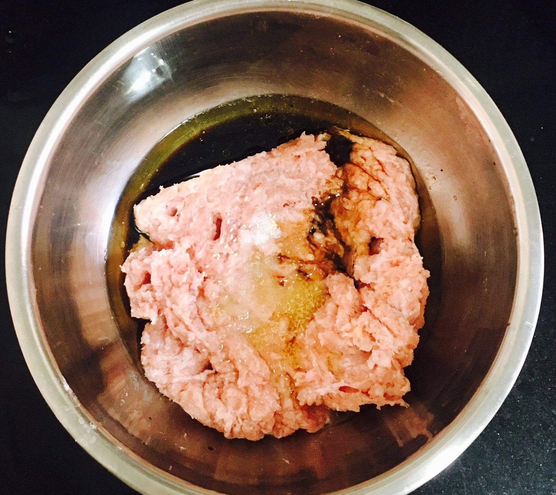 一名厨师正在厨房中使用不锈钢漏斗将粉红色肉馅灌入透明湿润的猪肠衣中,操作台整洁,旁边放有切好的红蒜丁和调味碗 手工灌制蒜香红肠过程