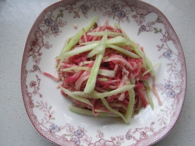 一盘色彩鲜艳的凉拌蔬菜沙拉,包含黄色胡萝卜丝、绿色黄瓜丝、紫色紫甘蓝和红色樱桃番茄,表面淋有光泽的酱汁,撒有白芝麻和绿色薄荷叶,摆放在白色瓷盘中 蔬菜沙拉成品图