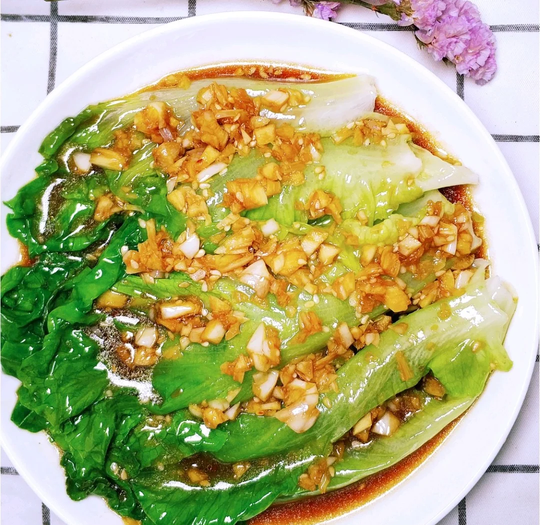 成品家常蚝油生菜特写:翠绿的散叶生菜整齐码放在雪白圆盘中央,表面覆盖一层晶莹透亮的琥珀色酱汁,零星分布着金黄色蒜粒,边缘点缀红色细椒丝,整体光泽诱人,背景虚化,突出食物主体 图片描述
