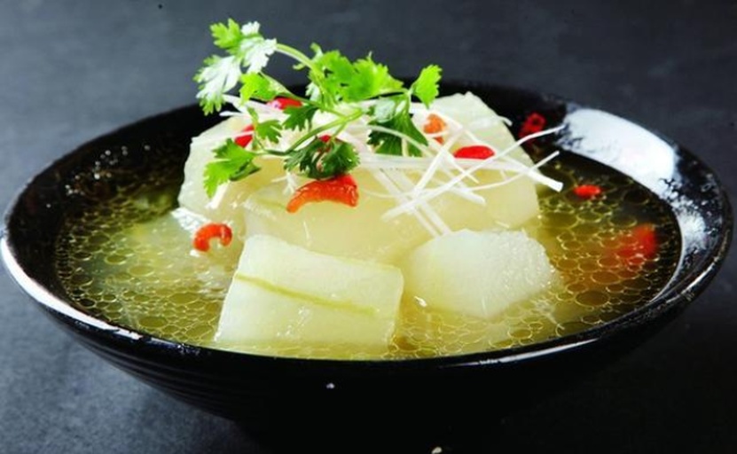 白瓷碗中盛有热腾腾的冬瓜豆腐汤,表面漂浮葱花,汤色清亮,展现成品美观与食欲感 一碗盛好的冬瓜豆腐汤特写,配有葱花点缀,放置在木质餐桌上,背景模糊,营造温馨用餐氛围