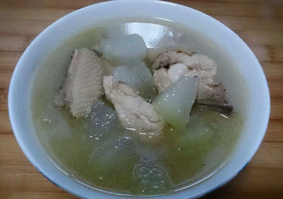 一口黑色铁锅中正在翻炒的冬瓜与鸡肉混合食材,色泽清亮,冬瓜呈半透明状,鸡肉泛着油光,旁边放有酱油瓶、蒜瓣和葱段,体现中式快炒过程的真实感 图片描述