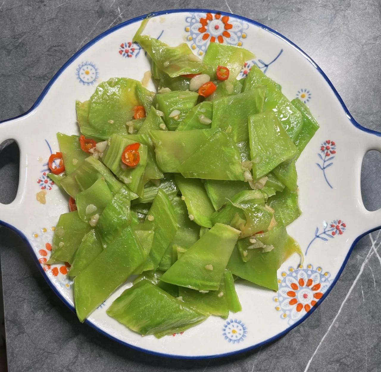 中式家庭厨房实景:茎用莴苣切片急火快炒过程,突出‘短时高温’工艺特征,展示无动物性食材、少油、保色保脆的健康烹饪方式 家庭厨房场景:不锈钢炒锅中莴笋片正在急火快炒,莴笋呈鲜亮翠绿色,边缘微透明,锅气升腾,配蒜末与少量植物油,无肉类配料