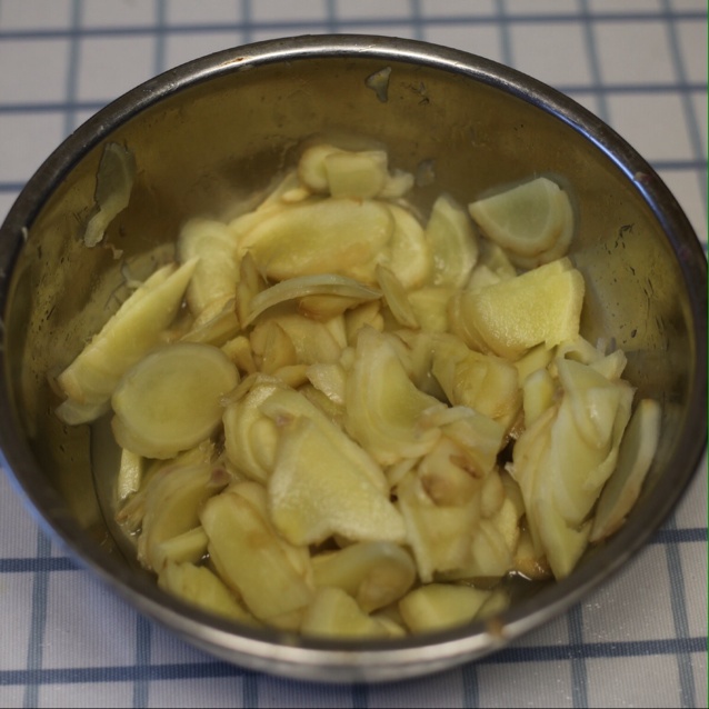 一位厨师正在陶瓷锅中慢火熬煮大黄姜片,锅中水汽升腾,旁边摆放着新鲜姜块、茶杯和木勺,台面上铺有竹制厨具垫,整体氛围温暖舒适 厨房中正在熬制姜茶的场景