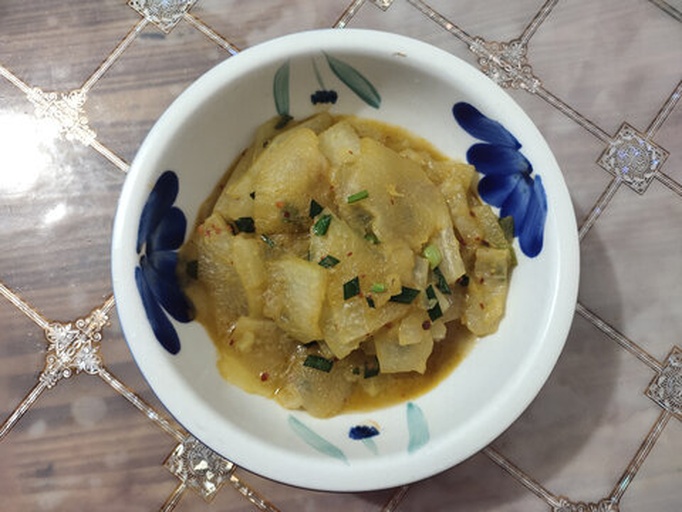平底锅中翻炒着橙红色的韩式辣酱白萝卜，锅铲正在翻动食材，旁边放有韩式辣酱瓶和蒜末碟