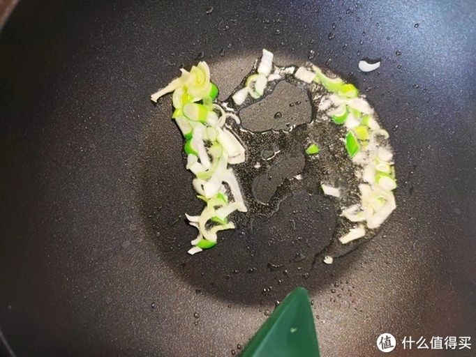 一位家庭主妇正在厨房切碎新鲜小葱,案板上有完整的葱段和已切好的葱花,旁边是一口正在加热的炒锅,锅中菜肴冒起轻烟,整体呈现温馨健康的家常烹饪氛围 家庭厨房中使用小葱烹饪的场景