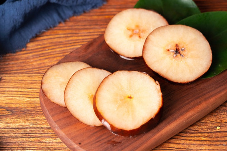 一张木质餐桌上摆放着由6月酥梨制作的多种食品组合,包括一杯透明玻璃杯中的冰镇梨汁、一小碗炖梨甜品(配有枸杞和红枣)、一份水果沙拉中含有切片酥梨与其他水果,整体风格清新自然,背景虚化的厨房环境透出温暖灯光 6月酥梨制作的饮品与甜品拼盘