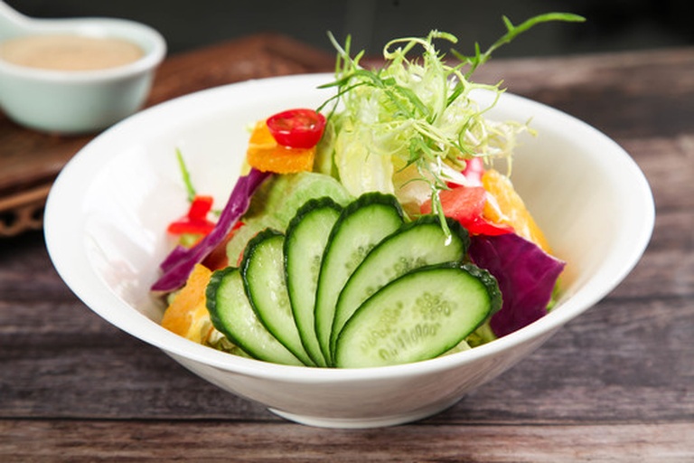 一碗色彩丰富的番茄蔬菜沙拉特写，包含切片西红柿、黄瓜、紫洋葱、生菜和橄榄油淋面，旁边放有一把木勺