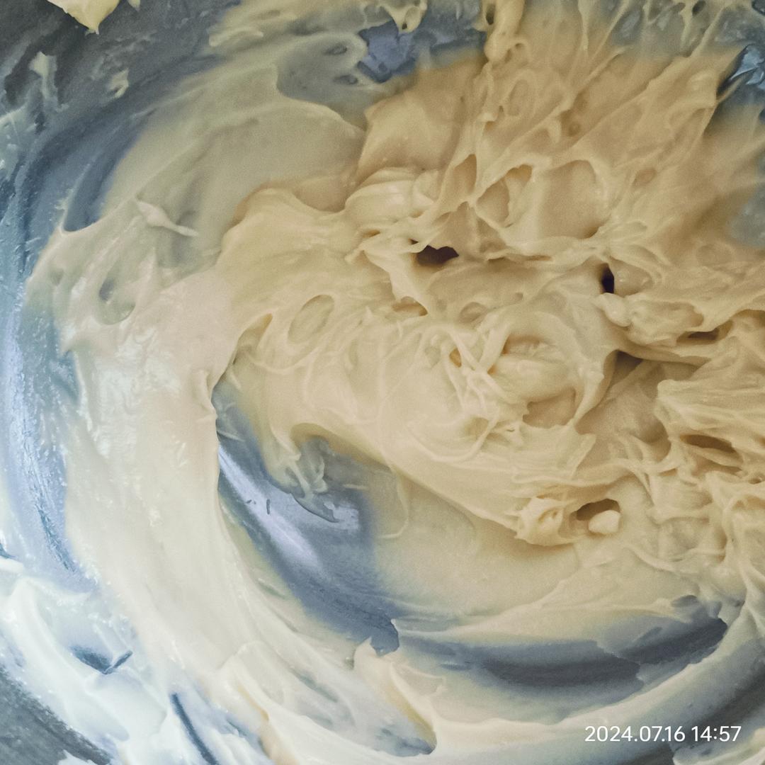 芝士奶油混合过程特写,展示正确的翻拌手法与理想质地 厨师正在用硅胶刮刀将打发淡奶油与奶油奶酪混合,动作轻柔呈“J”字翻拌,碗中呈现乳白色蓬松奶油质地