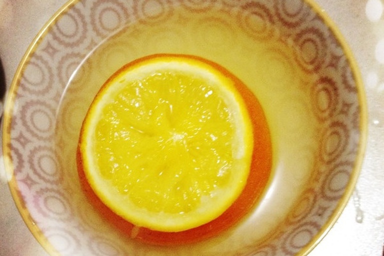 烤箱内部视角,两个橙色的橙碗整齐排列在白色烤盘上,表面微微冒泡,边缘略带焦黄色,散发出温暖的光晕。周围可见少量蒸汽升腾,背景为烤箱加热管发出的橙红色光芒 烤箱中的烤甜橙