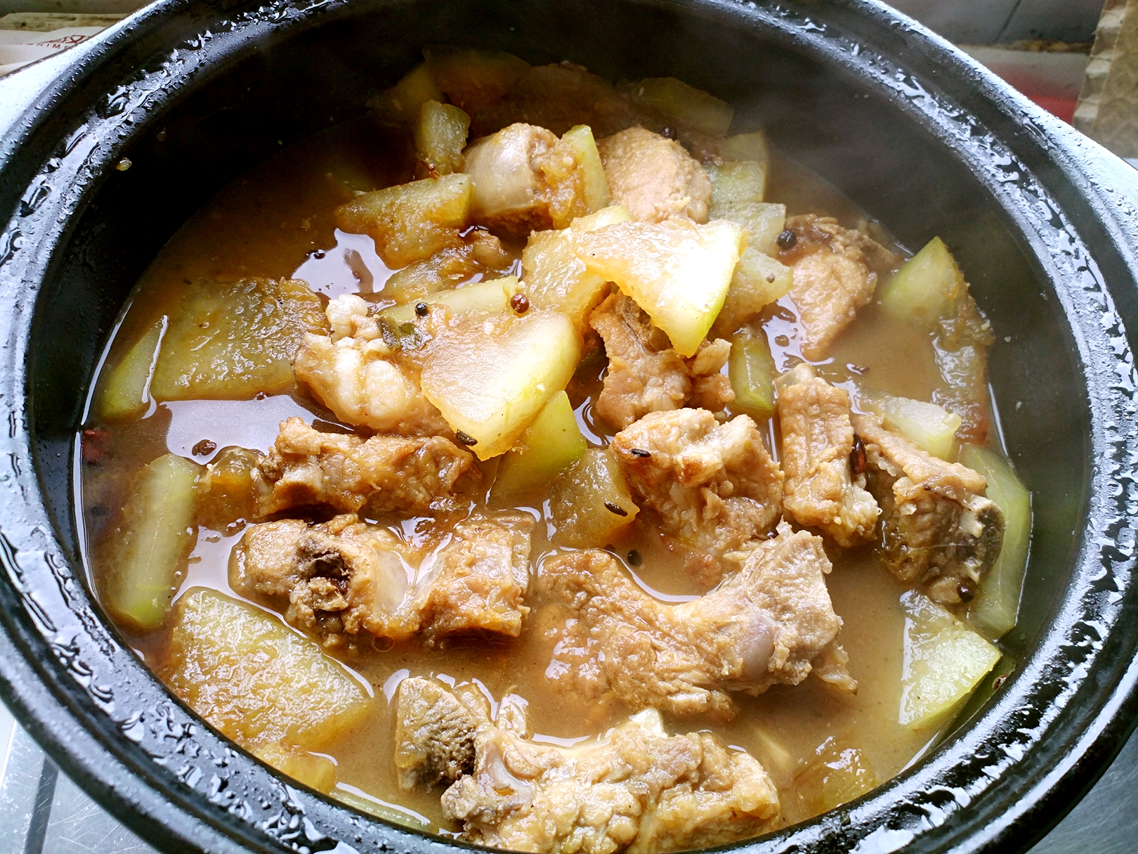 砂锅内正在炖煮的猪肉冬瓜,汤汁呈浅褐色,食材分布均匀,热气蒸腾,体现菜肴的温暖质感和浓郁香气 正在炖煮中的猪肉冬瓜,锅中汤汁微沸,冬瓜块半透明,猪肉片浮于表面,蒸汽袅袅上升
