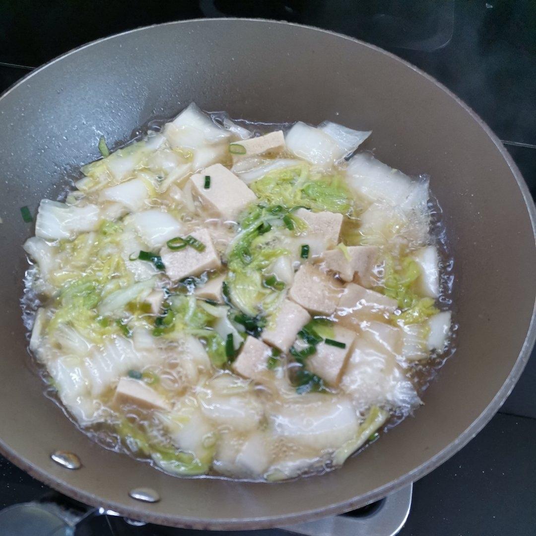 不锈钢炒锅中正在炖煮白菜炖豆腐,可见白菜帮已半透明,豆腐块完整漂浮在乳白色汤汁中,锅边有姜片和葱段,炉火为中小火,蒸汽缓缓升起,背景为整洁厨房环境 烹饪过程图