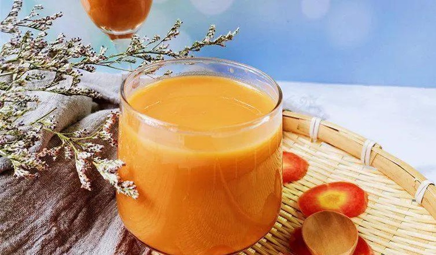 一杯橙绿色混合果蔬汁放置在白色托盘上，旁边摆放胡萝卜条、芹菜段和柠檬片，背景为简约厨房风格