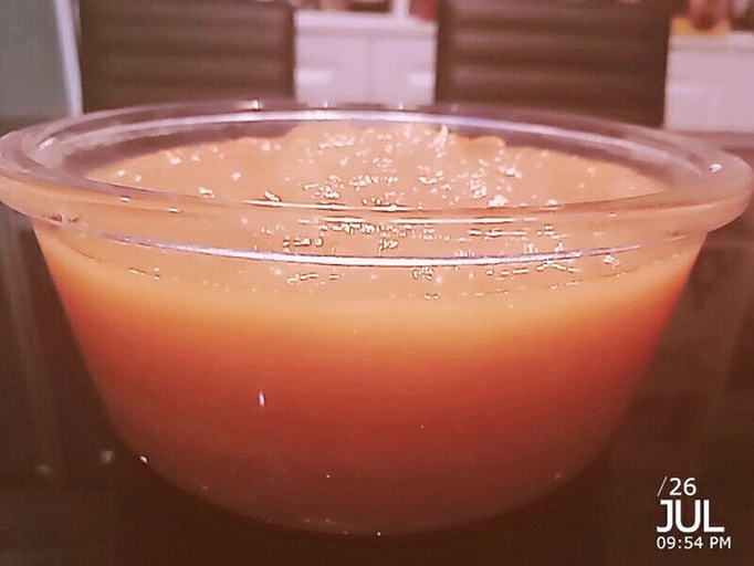 一个透明玻璃碗中放置着一只被切开顶部的橙子,内部可见嵌入少许白色晶体状食盐,旁边摆放一把小勺和一双筷子,背景为厨房灶台上的蒸锅,热气袅袅升起 盐蒸橙子制作过程