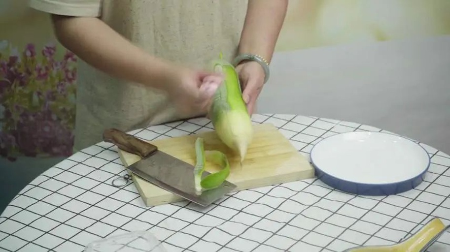 一位厨师正在厨房操作台上用流动清水冲洗一根新鲜白皮萝卜,随后用不锈钢削皮刀去除外皮,案板旁摆放着切好的萝卜块和工具 新鲜白皮萝卜清洗与去皮过程