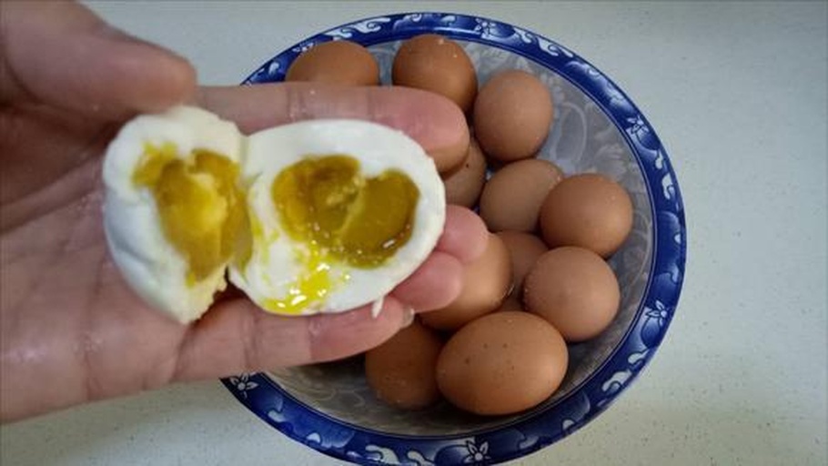 不粘锅中正在中小火加热,锅内有少量食用油,咸鸭蛋黄被压碎后在锅中翻炒,表面开始冒小泡并析出橙红色油脂,周围有轻微烟气,旁边放有一把木铲 咸鸭蛋黄煸炒过程