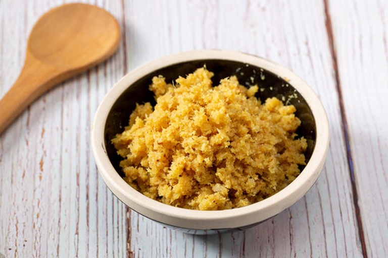 一个白色陶瓷碗中盛有金黄色的天然蜂蜜,旁边撒有一勺淡黄色的面姜粉末,正在用木勺搅拌混合,两者逐渐融合成均匀的糊状物,背景为木质餐桌和新鲜生姜片 面姜粉与蜂蜜混合过程特写