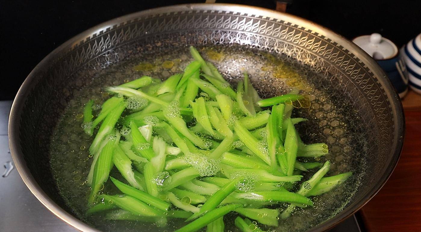 一锅沸腾的清水正在焯烫一把新鲜香芹,香芹呈翠绿色,正在水中翻滚,旁边放着漏勺和冰水碗,用于迅速冷却 香芹焯水过程特写