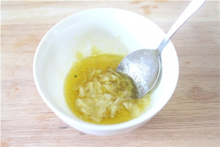 一盘刚出锅的意式蒜香橄榄油拌面，面条裹满金黄色蒜油汁，表面点缀焦香蒜片与红色辣椒碎，旁边放着一只木柄蒜杵和空石臼，体现从原料到成菜的全过程