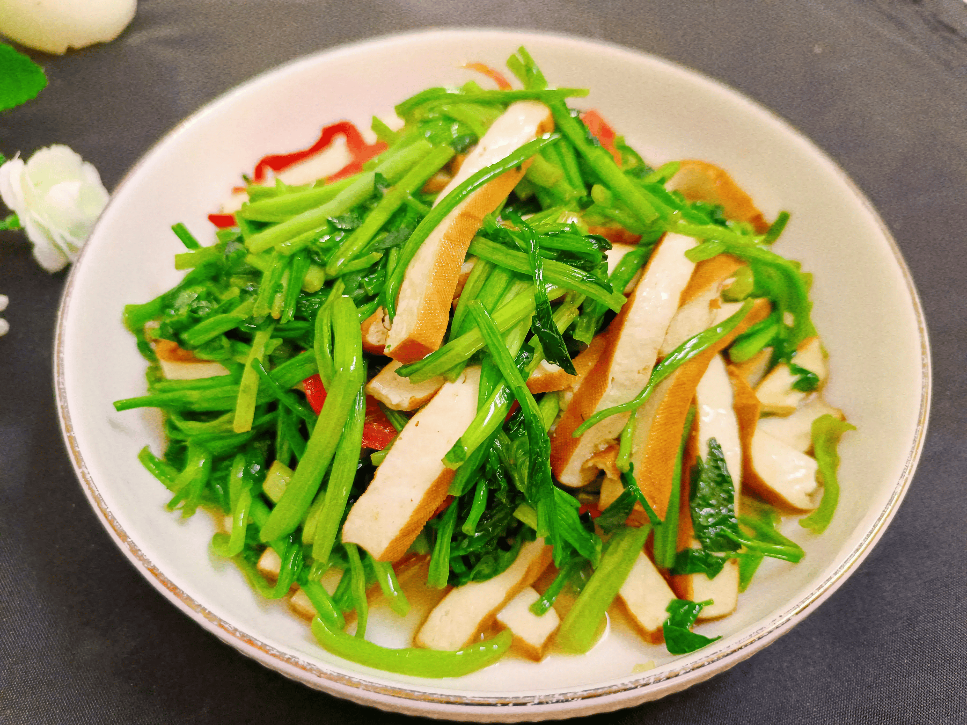 高清俯拍:翠绿茼蒿段与乳白北豆腐丁相间分布,豆腐表面微焦呈金黄色,锅底有少量琥珀色酱汁,背景为青花瓷浅盘,体现中式家常烹饪质感 茼蒿炒北豆腐特写