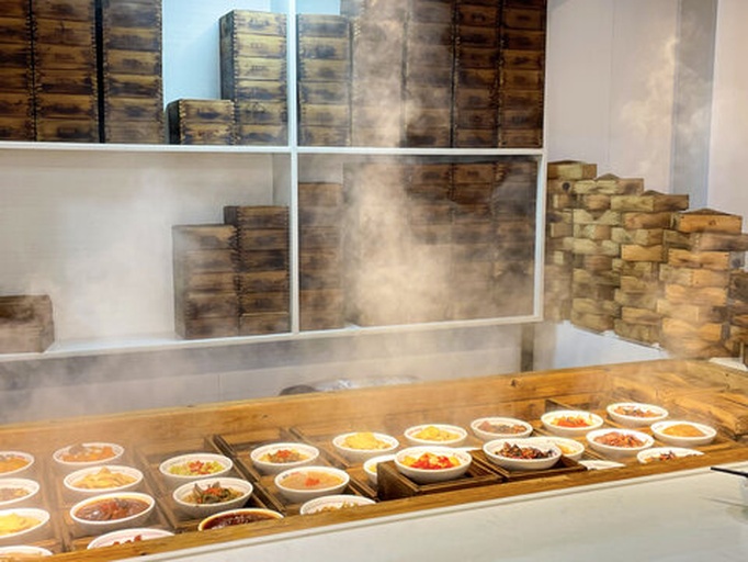 一个传统的中式蒸锅正在工作,蒸汽袅袅升起,上方的竹蒸笼里整齐铺放着深紫色的五味子果实,旁边摆放着一个小酒壶和量勺,显示黄酒添加过程,整体画面温馨自然,突出手工制作感 蒸制过程展示图