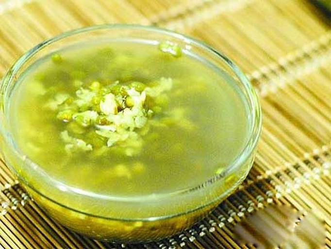 俯拍视角:不锈钢锅中盛放刚煮好待冷却的绿豆汤(浅绿色液体,可见少量完整绿豆沉底),旁边置玻璃量杯(内盛约10mL鲜榨柠檬汁)、陶瓷小勺、电子温度计(屏幕显示38.5℃),操作台面整洁,体现‘精准、可控、家庭可执行’的核心要点 家庭厨房操作场景图