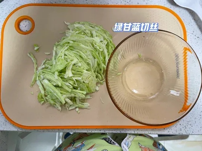 一双戴着食品手套的手正在将绿甘蓝的叶片一片片用手撕成适口大小,菜叶散落在白色砧板上,背景中有炒锅和调料瓶,体现真实的厨房操作场景 厨房中正在手撕甘蓝的过程