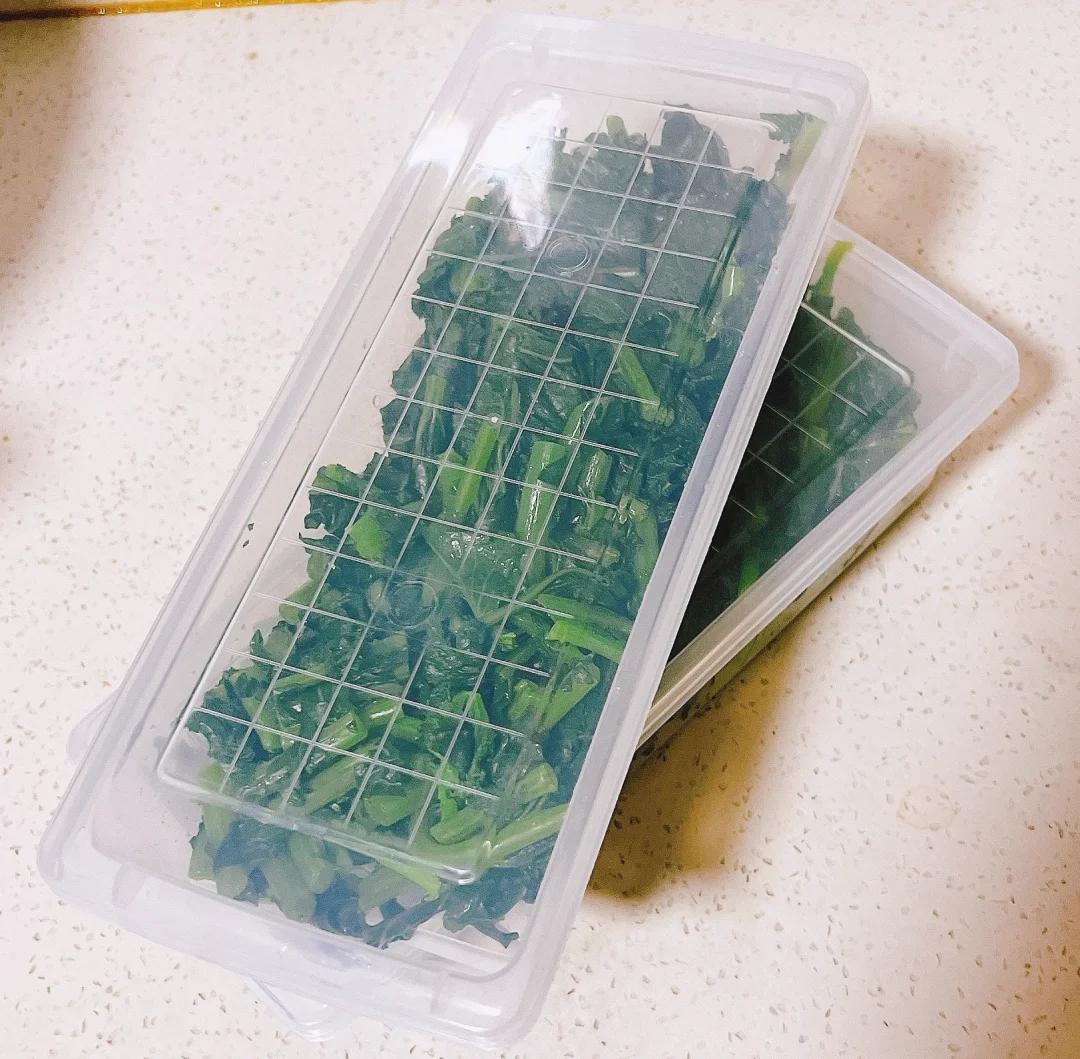 一个透明的长方形塑料储物盒内,多片翠绿的生菜叶被白色厨房纸巾层层隔开,盒子部分打开,放置在冰箱冷藏室的果蔬抽屉中央,周围空间整洁,无其他杂物干扰 透明塑料收纳盒中整齐码放着用纸巾包裹的生菜叶,盒子半开,位于冰箱蔬果层中央位置