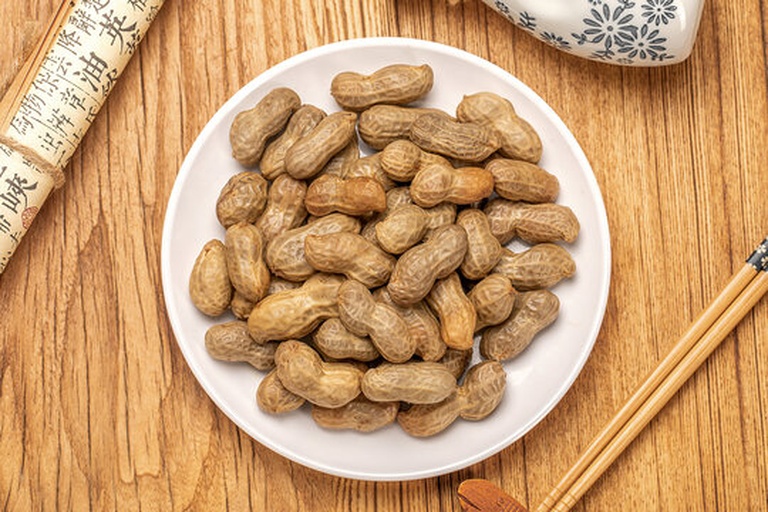 一盘去壳的生花生,颗粒饱满,呈浅米黄色,表面有网状纹理,背景为木质餐桌,体现自然健康的饮食氛围 花生特写照片